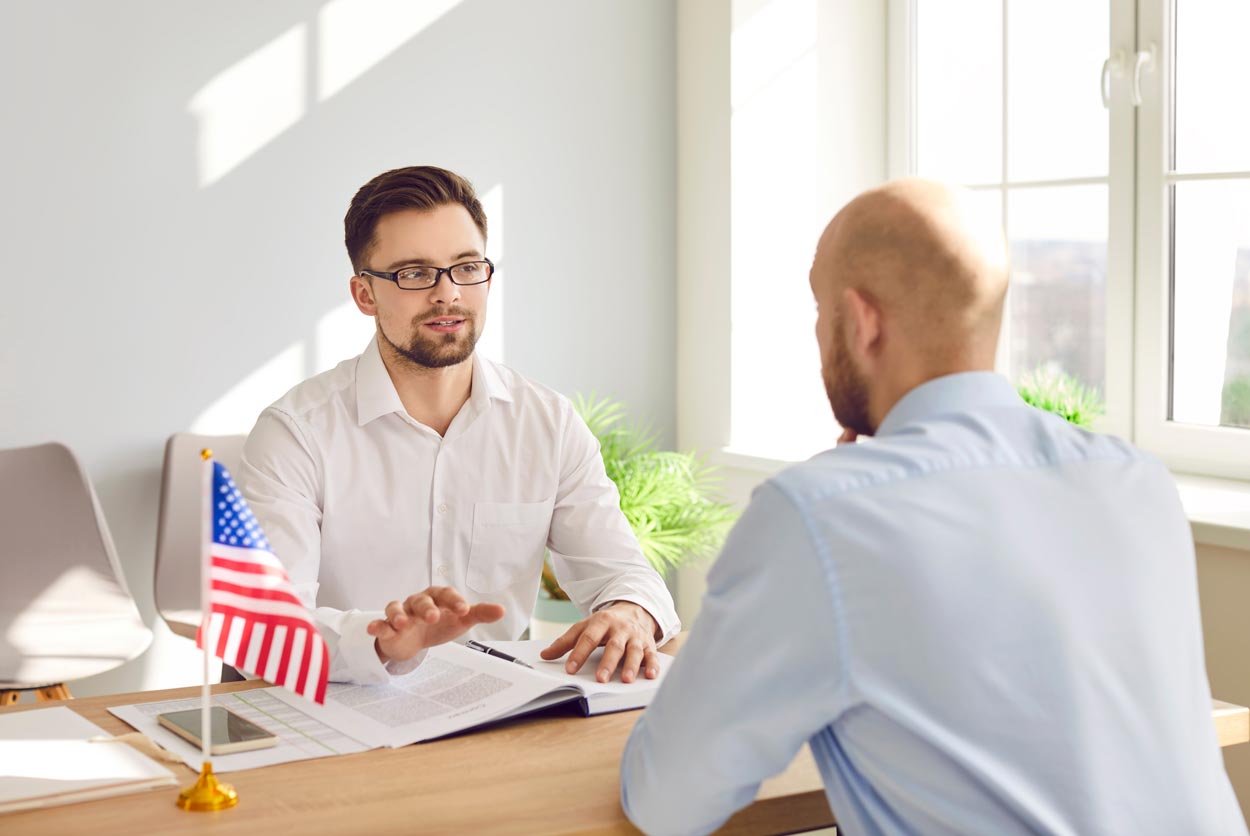 Serious male sitting at office table with American flag and documents